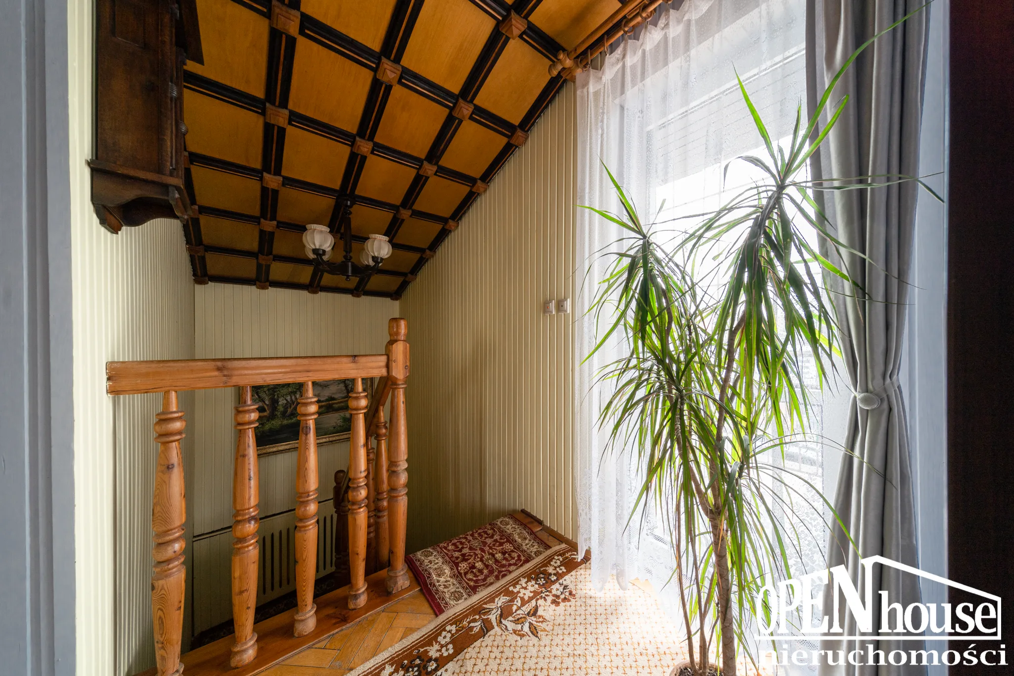 Dom na sprzedaż Białogard – ul. Szymanowskiego 6 | 149,30 m² | ogród zimowy | garaż 24 Przestronne wnętrze mieszkania z dużym oknem, roślinami i drewnianymi elementami, idealne do organiz.